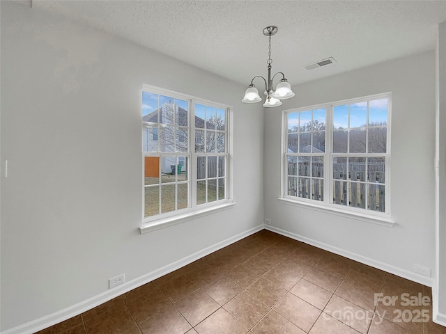 unfurnished dining area with plenty of natural light, dark tile patterned flooring, a chandelier, and a textured ceiling