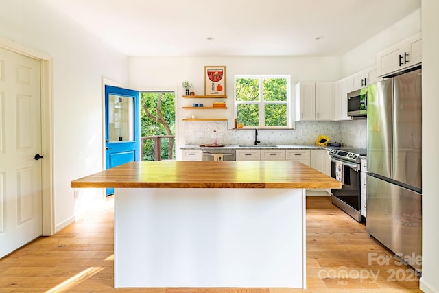 kitchen with butcher block counters, stainless steel appliances, a center island, and white cabinets