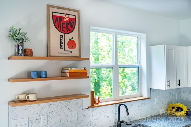 interior details with tasteful backsplash, white cabinetry, and stone countertops