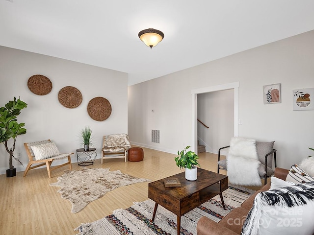 living room with light wood-type flooring, visible vents, stairway, and baseboards