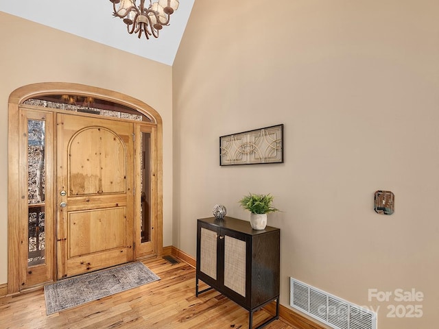 foyer entrance featuring light wood-style floors, baseboards, visible vents, and a chandelier