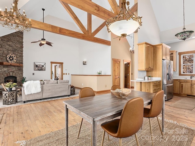 dining area featuring ceiling fan with notable chandelier, light wood-type flooring, a fireplace, and high vaulted ceiling