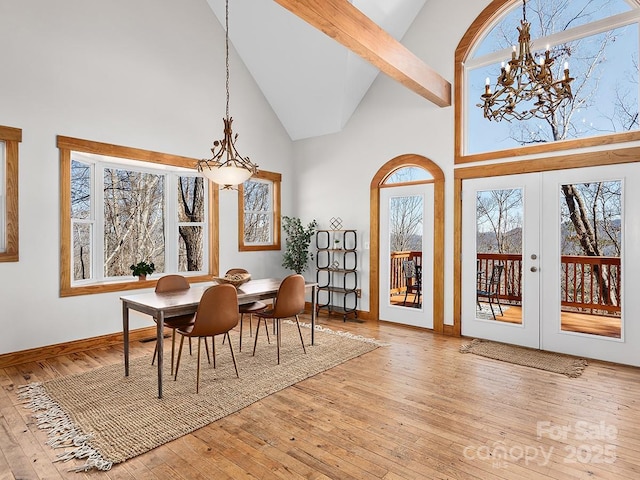 dining space with high vaulted ceiling, a notable chandelier, baseboards, french doors, and hardwood / wood-style floors