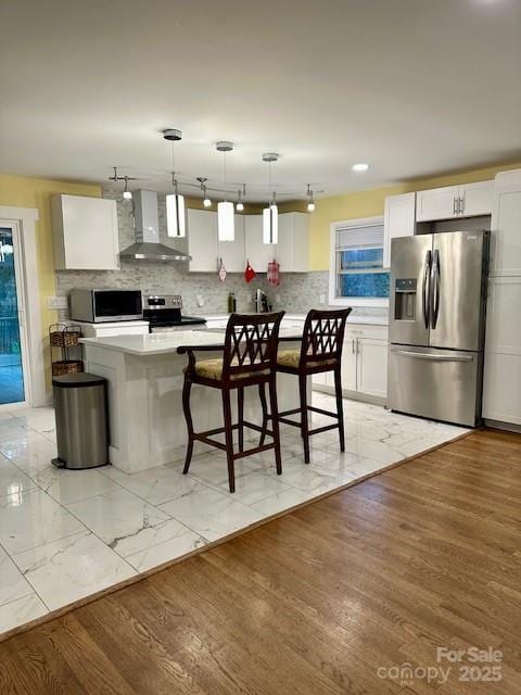 kitchen featuring wall chimney range hood, backsplash, appliances with stainless steel finishes, white cabinets, and light countertops