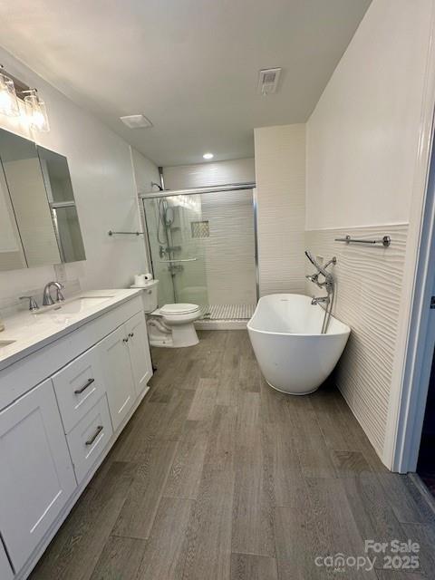 bathroom with a stall shower, toilet, wood finished floors, and vanity