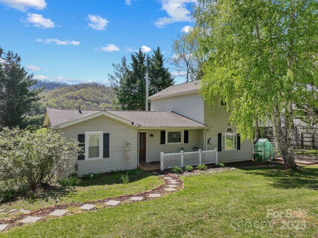 view of front of property featuring a front lawn, a mountain view, fence, and a shingled roof