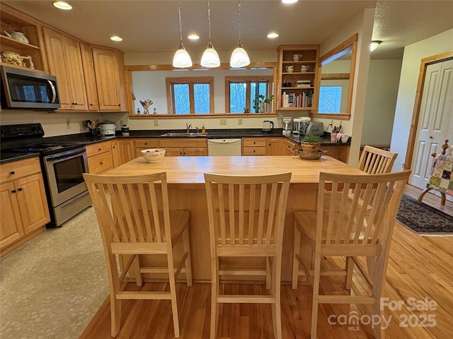 kitchen with sink, hanging light fixtures, stainless steel appliances, a kitchen breakfast bar, and wood counters