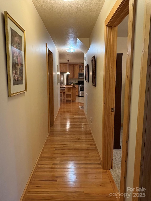 hall with a textured ceiling and light hardwood / wood-style flooring