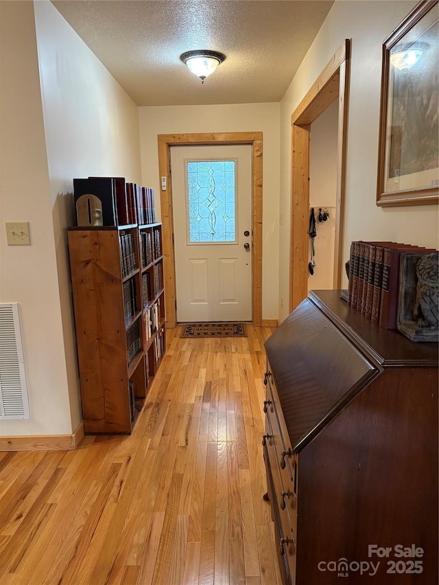 doorway to outside featuring a textured ceiling and light hardwood / wood-style flooring