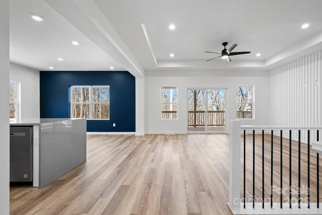 unfurnished living room with a raised ceiling, ceiling fan, and light hardwood / wood-style floors