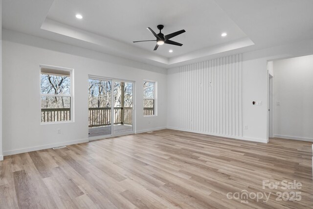 spare room with a raised ceiling, ceiling fan, and light wood-type flooring