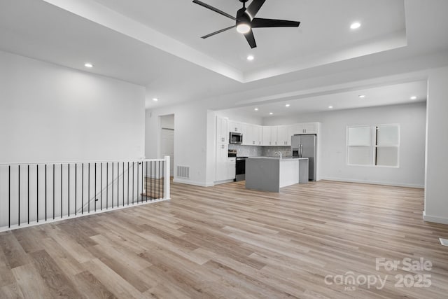 unfurnished living room with a tray ceiling, ceiling fan, and light hardwood / wood-style flooring