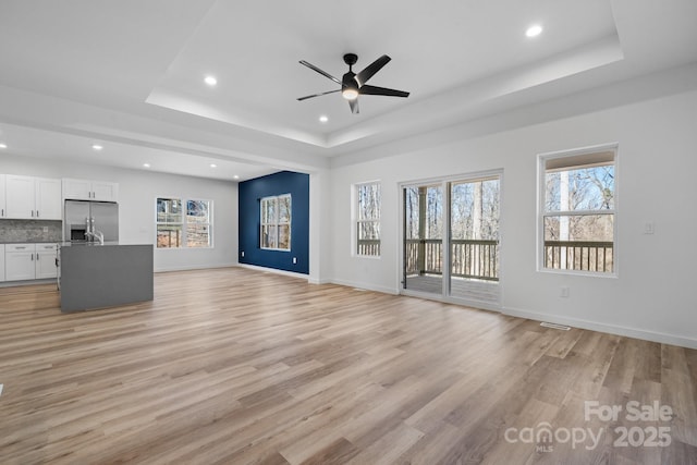 unfurnished living room featuring a healthy amount of sunlight, light hardwood / wood-style floors, and a tray ceiling