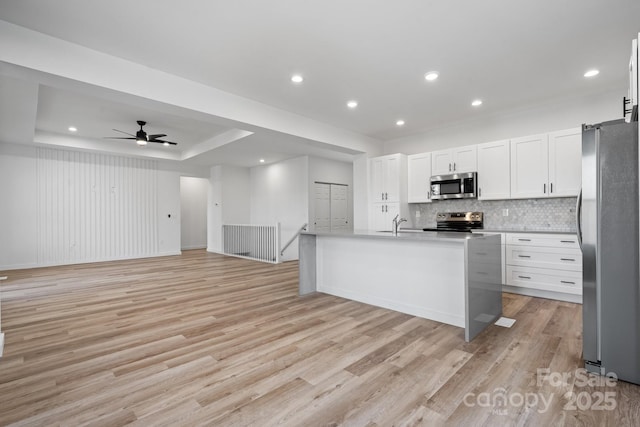 kitchen featuring stainless steel appliances, white cabinetry, an island with sink, and light hardwood / wood-style floors