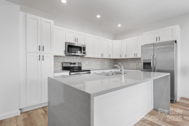 kitchen featuring stainless steel appliances, sink, white cabinets, and a kitchen island with sink