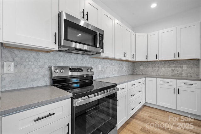 kitchen with tasteful backsplash, light hardwood / wood-style floors, white cabinets, and appliances with stainless steel finishes