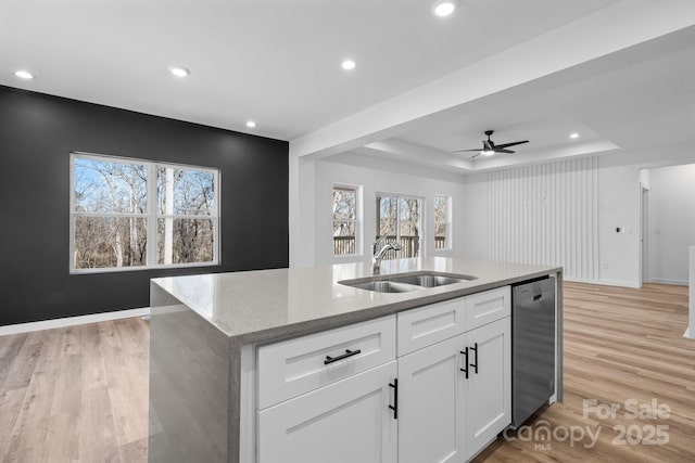 kitchen with white cabinetry, sink, stainless steel dishwasher, a tray ceiling, and a center island with sink