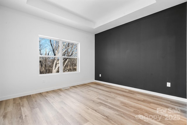 spare room featuring light wood-type flooring and a tray ceiling