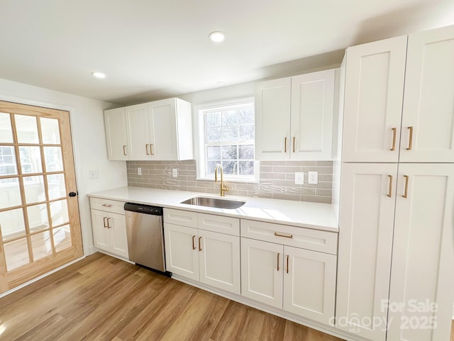 kitchen with dishwasher, light wood-style flooring, a sink, and white cabinetry