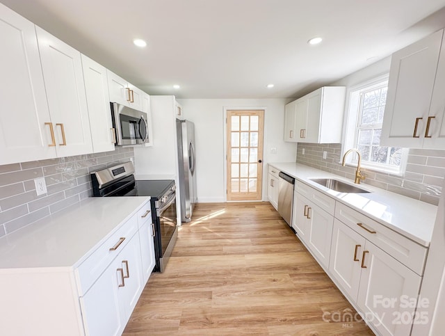 kitchen featuring white cabinets, a sink, stainless steel appliances, and light wood finished floors