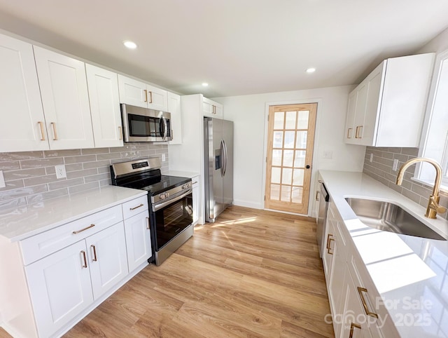 kitchen with white cabinets, a sink, light wood-style floors, and appliances with stainless steel finishes