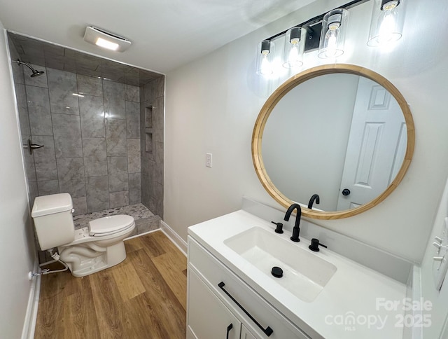 full bathroom featuring toilet, tiled shower, vanity, wood finished floors, and baseboards