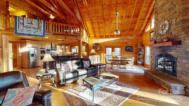 living room with a stone fireplace, wood ceiling, wooden walls, and light hardwood / wood-style floors