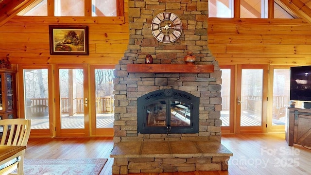 unfurnished living room featuring a stone fireplace, wooden walls, high vaulted ceiling, light wood-type flooring, and french doors