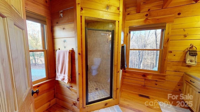 bathroom featuring a wealth of natural light, a shower with shower door, and wood walls