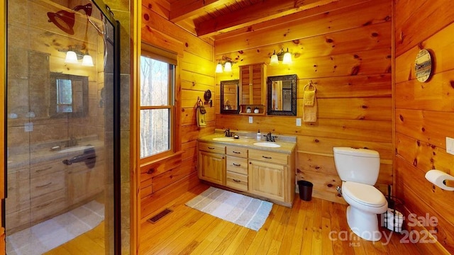 bathroom with hardwood / wood-style floors, wooden walls, a shower with shower door, vanity, and toilet