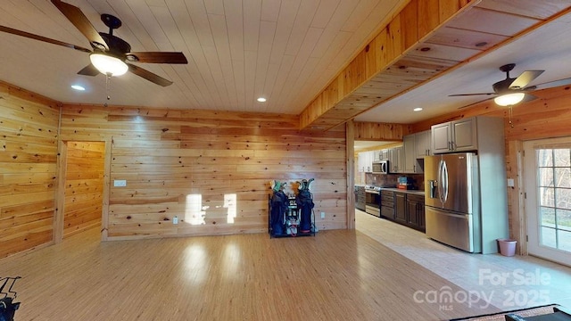 kitchen with wooden walls, light hardwood / wood-style floors, ceiling fan, and appliances with stainless steel finishes