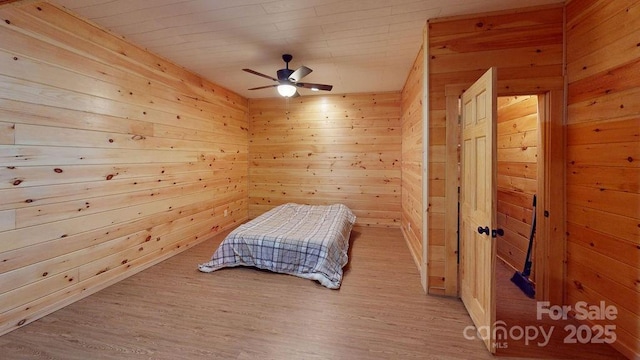 bedroom featuring light hardwood / wood-style flooring, ceiling fan, and wood walls