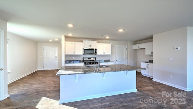 kitchen featuring appliances with stainless steel finishes, an island with sink, sink, white cabinets, and dark stone counters