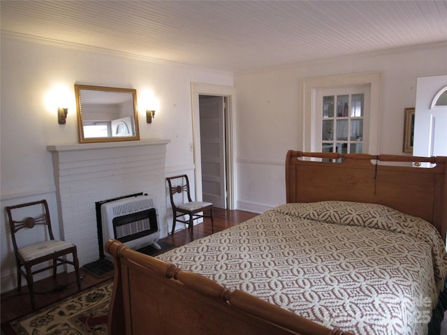 bedroom with heating unit, ornamental molding, dark wood-type flooring, and a brick fireplace