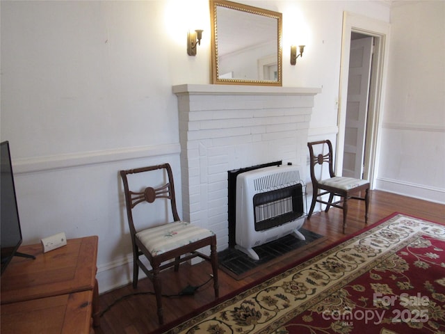 living area with heating unit, wainscoting, and wood finished floors