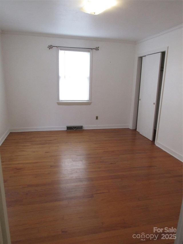 empty room featuring light wood-style flooring, ornamental molding, baseboards, and visible vents