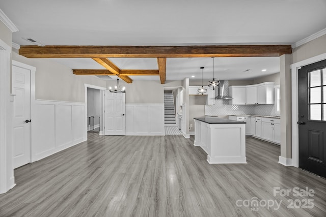 kitchen featuring pendant lighting, wall chimney range hood, a chandelier, white cabinets, and beamed ceiling