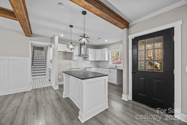 kitchen featuring wall chimney exhaust hood, pendant lighting, white cabinetry, a kitchen island, and beamed ceiling