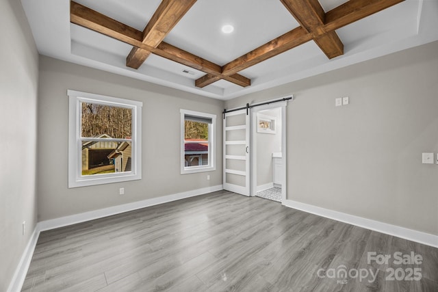 unfurnished bedroom with coffered ceiling, connected bathroom, beam ceiling, a barn door, and light hardwood / wood-style floors