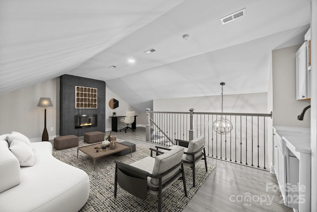 living room featuring a tile fireplace, vaulted ceiling, an inviting chandelier, and light hardwood / wood-style flooring