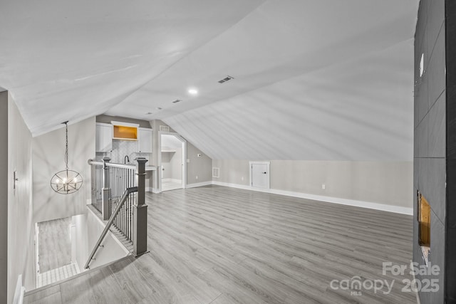 bonus room with hardwood / wood-style floors, vaulted ceiling, and a chandelier