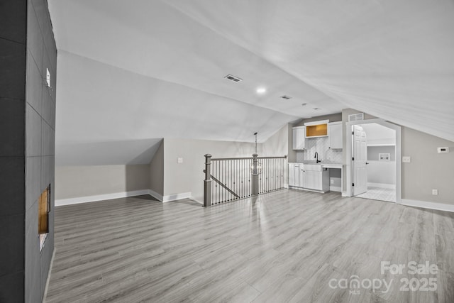 additional living space featuring vaulted ceiling, sink, and light hardwood / wood-style floors