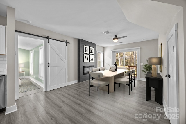 dining room with ceiling fan, a barn door, a tiled fireplace, and light wood-type flooring