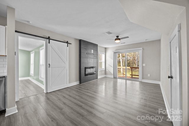 unfurnished living room with ceiling fan, a barn door, a fireplace, and light hardwood / wood-style floors