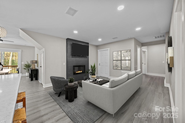 living room with ceiling fan, a large fireplace, and light wood-type flooring