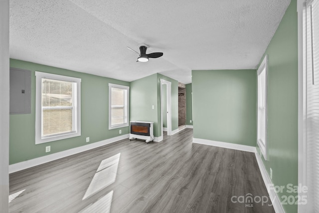 unfurnished living room featuring heating unit, hardwood / wood-style floors, electric panel, ceiling fan, and a textured ceiling