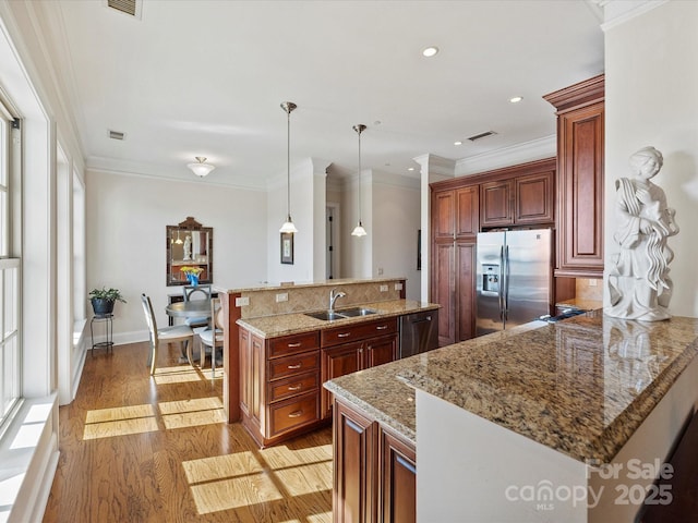 kitchen featuring sink, hanging light fixtures, light wood-type flooring, ornamental molding, and appliances with stainless steel finishes