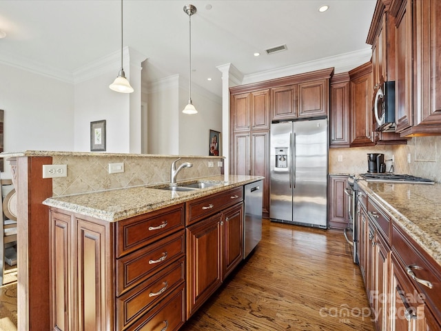 kitchen with hardwood / wood-style flooring, appliances with stainless steel finishes, a kitchen island with sink, light stone countertops, and decorative light fixtures