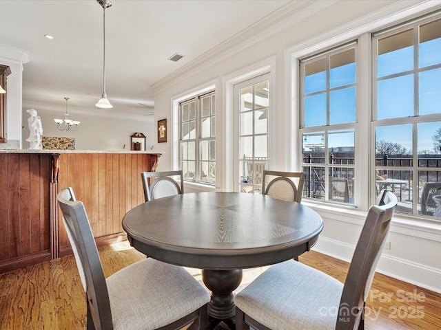 dining space with ornamental molding, an inviting chandelier, and light hardwood / wood-style floors