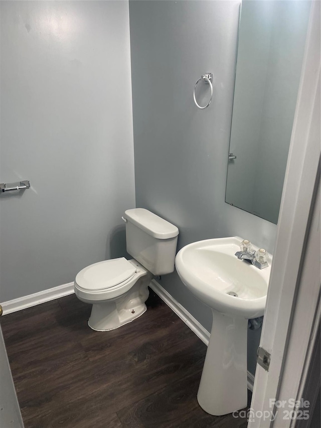 half bath with baseboards, toilet, and wood finished floors